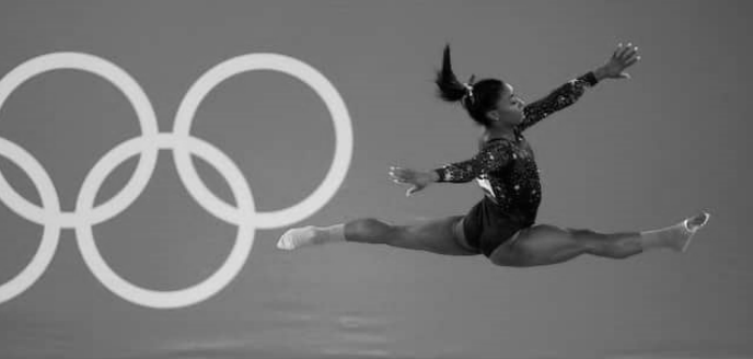 Turnerin im weiten Spagat-Sprung vor Olympischen Ringen